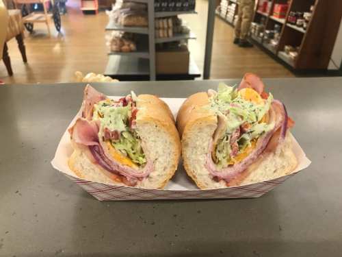 A close-up of two sandwiches filled with ham, lettuce, and other toppings, served on a paper tray.