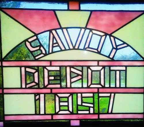 Stained glass window featuring the words "Savoy Depot 1897" in colorful geometric patterns.