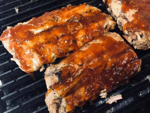 Grilled ribs coated in a shiny barbecue sauce, sizzling on a barbecue grill.