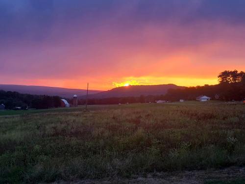 A vibrant sunset over rolling hills, with a field in the foreground and a silhouette of a barn in the distance.