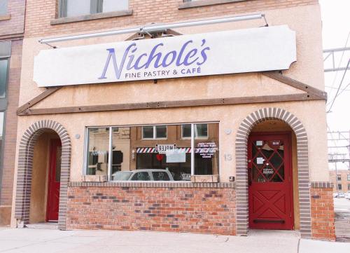 Exterior of Nichole's Fine Pastry & Café, featuring a brick facade and red doors, with a large sign above the window.