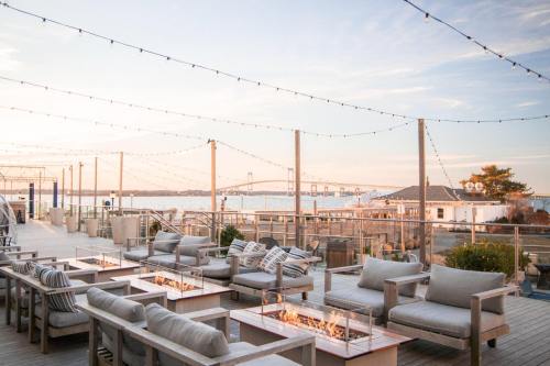 A cozy outdoor lounge area with fire pits, overlooking a waterfront at sunset, adorned with string lights.