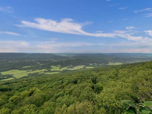 A panoramic view of lush green valleys and rolling hills under a blue sky with scattered clouds.