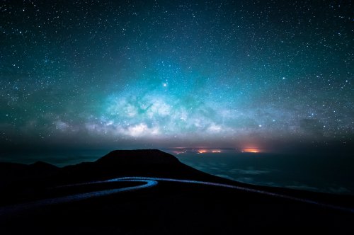 A starry night sky with the Milky Way over a dark landscape, featuring distant lights on the horizon.