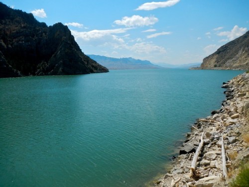 A serene lake surrounded by rocky hills under a clear blue sky, with gentle waves lapping at the shore.