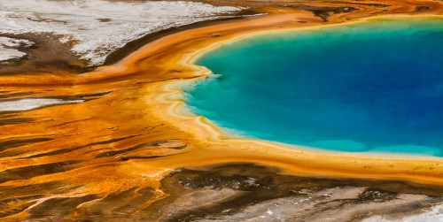 Aerial view of a vibrant hot spring with bright blue water surrounded by orange and yellow mineral deposits.