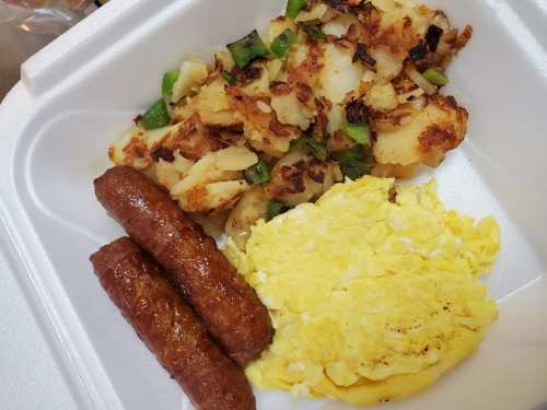 A takeout container with scrambled eggs, sausage links, and crispy hash browns with green peppers.