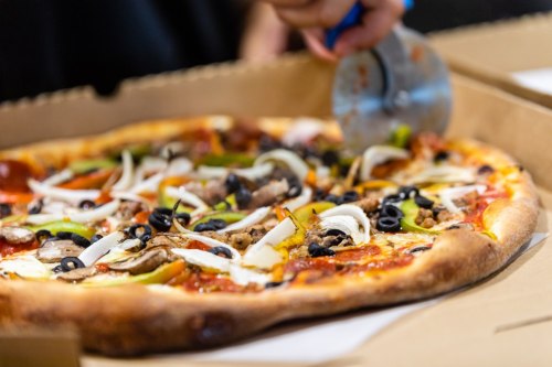 A close-up of a pizza with various toppings being sliced with a pizza cutter.