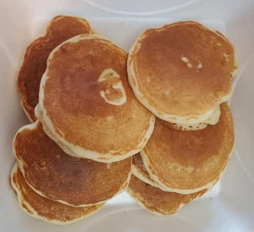 A stack of golden-brown pancakes arranged in a white container.