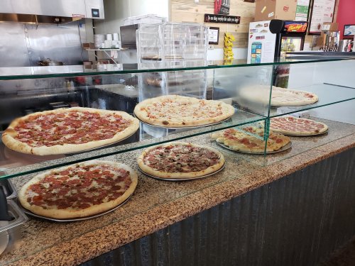 A display case with various pizzas, including pepperoni, cheese, and meat toppings, in a casual eatery.
