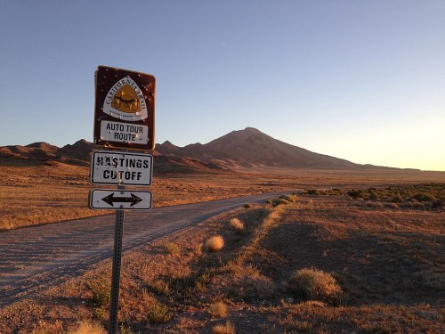 A road sign for an auto tour route with a mountain in the background during sunset in a desert landscape.