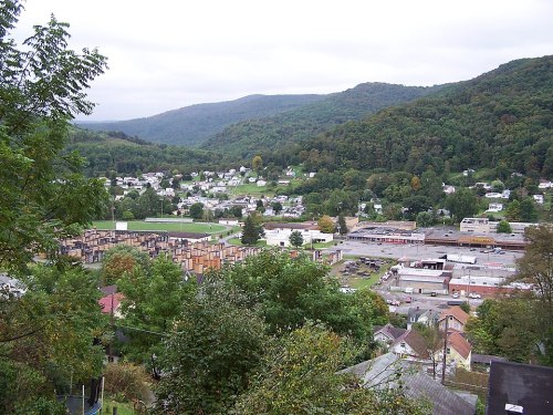 A scenic view of a small town nestled in green hills, with buildings and a train yard visible in the foreground.