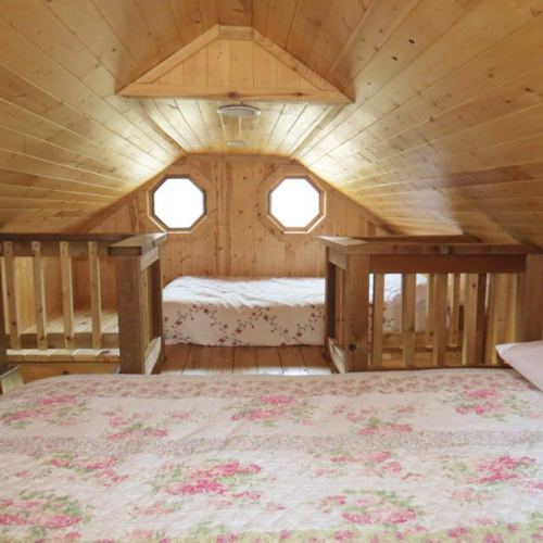 Cozy wooden attic with two beds, floral bedding, and octagonal windows, creating a warm, inviting atmosphere.