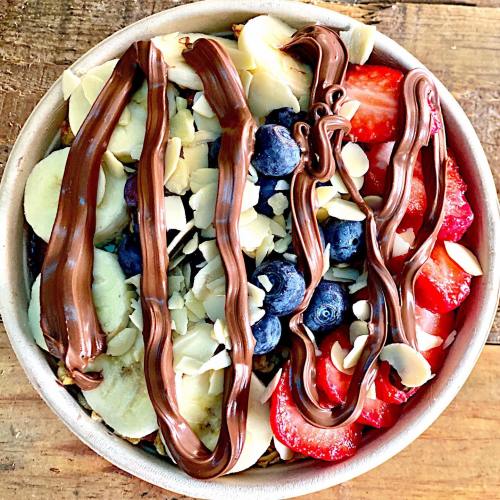 A bowl of fruit topped with sliced bananas, strawberries, blueberries, almond slices, and drizzled with chocolate.