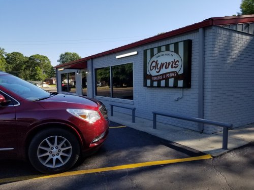 A red car parked in front of Glynn's Burgers & Po'boys, a gray building with a striped sign.