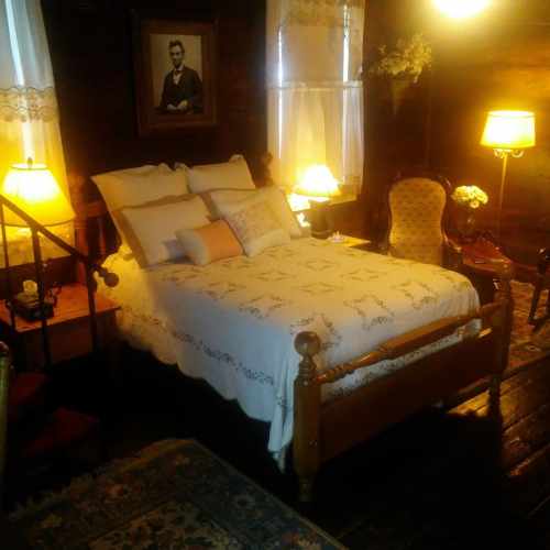 Cozy bedroom with a wooden bed, decorative pillows, vintage lamps, and a portrait on the wall. Warm, inviting atmosphere.