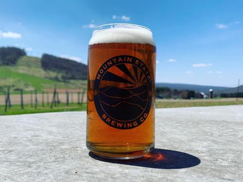 A glass of amber beer with a frothy head, set against a scenic landscape and blue sky.