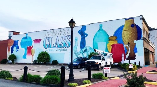 Colorful mural of glassware on the side of the Museum of American Glass in West Virginia, with a parked truck nearby.