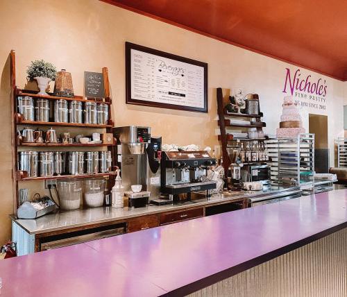 A cozy pastry shop counter with shelves of jars, a coffee machine, and a menu board on the wall.