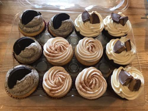 A tray of assorted cupcakes: some topped with Oreo cookies, others with swirls of frosting and chocolate pieces.