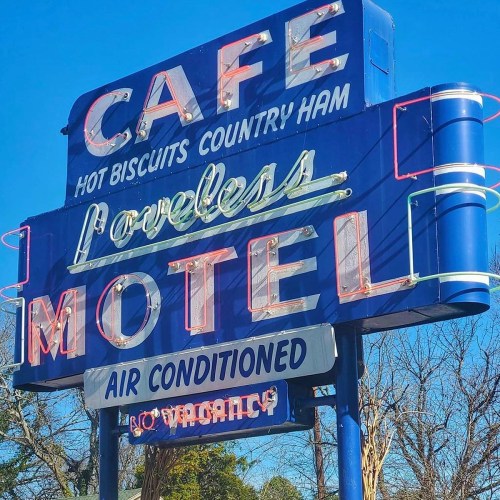 Bright blue sign for Loveless Motel and Cafe, featuring neon lights and text about hot biscuits and air conditioning.