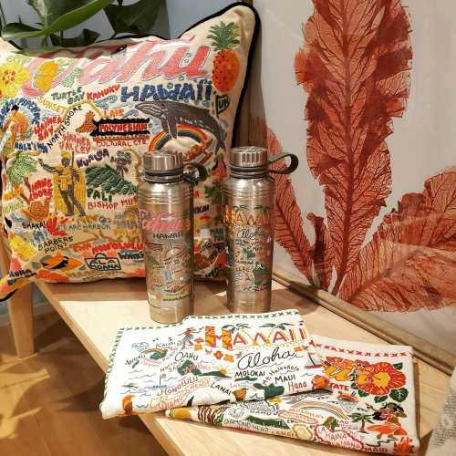Two decorative water bottles and a colorful pillow featuring Hawaiian designs, alongside a patterned cloth.