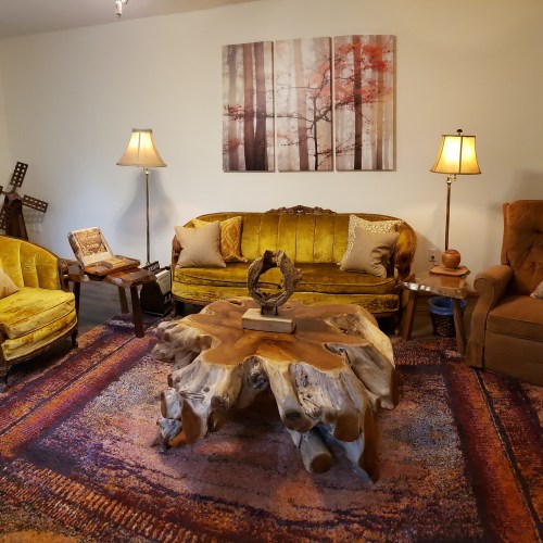 Cozy living room with vintage yellow sofa, wooden coffee table, and warm lighting, featuring a nature-themed wall art.