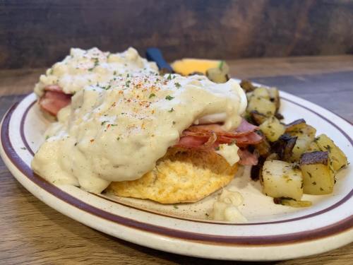 A plate of biscuits topped with creamy sausage gravy, served with seasoned diced potatoes on the side.