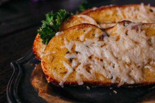 Toasted bread topped with melted cheese, garnished with parsley, served on a silver platter.