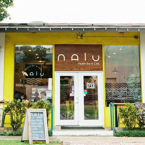 Exterior of Nalu Health Bar & Café, featuring a bright yellow facade, open sign, and outdoor seating.