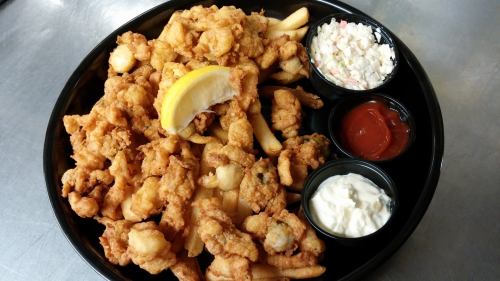 A plate of fried seafood, including shrimp and fish, served with fries, coleslaw, and dipping sauces.