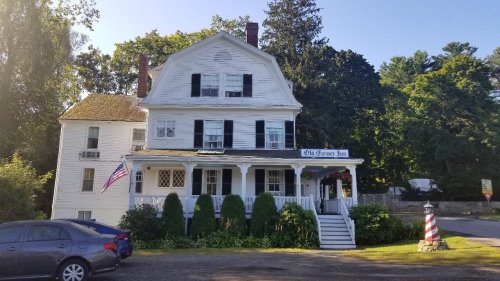 A large white house with a porch, American flag, and greenery, serving as the Old Grist Mill Inn.