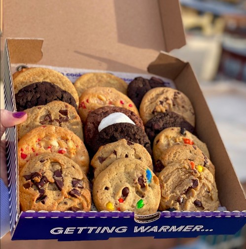 A box of assorted cookies, including chocolate chip, oatmeal, and colorful candy cookies, held by a hand.