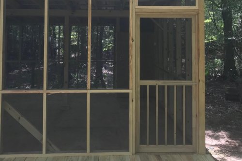 A partially constructed wooden structure with large windows, set in a wooded area.
