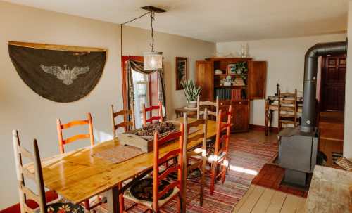 A cozy dining room with a wooden table, colorful chairs, a stove, and rustic decor. Warm and inviting atmosphere.