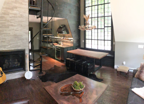 Modern living room with a spiral staircase, large windows, a fireplace, and a stylish dining table.