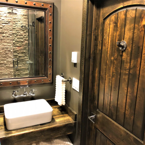 A rustic bathroom featuring a wooden door, stone wall, modern sink, and towel rack.