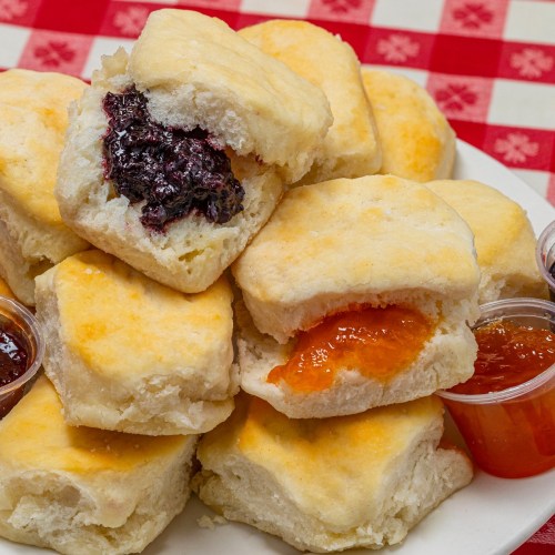 A plate of fluffy biscuits with jelly and jam, set on a red and white checkered tablecloth.