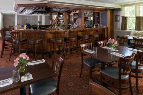 A cozy restaurant interior featuring a wooden bar, tables with flowers, and a warm, inviting atmosphere.