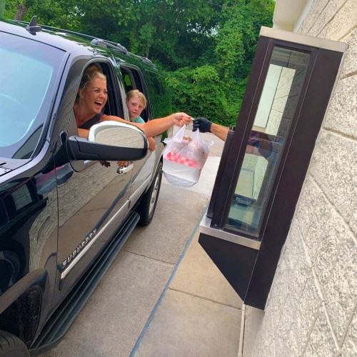A woman and a girl excitedly receive a takeout order from a drive-thru window.