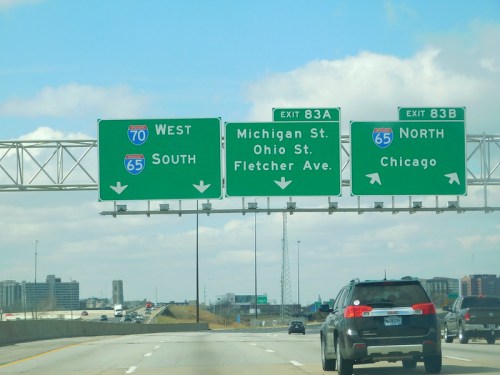 Highway exit signs for I-70 West, I-65 South, and I-65 North to Chicago, with clear blue sky in the background.