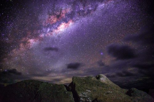 A stunning night sky filled with stars and the Milky Way, framed by dark rocky silhouettes in the foreground.