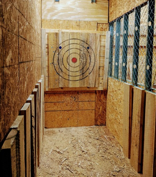 An indoor axe-throwing range with a wooden target and surrounding wooden walls.