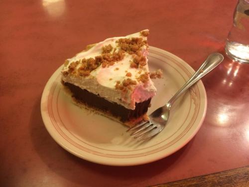A slice of chocolate cream pie topped with whipped cream and crumbled cookies on a plate, with a fork beside it.