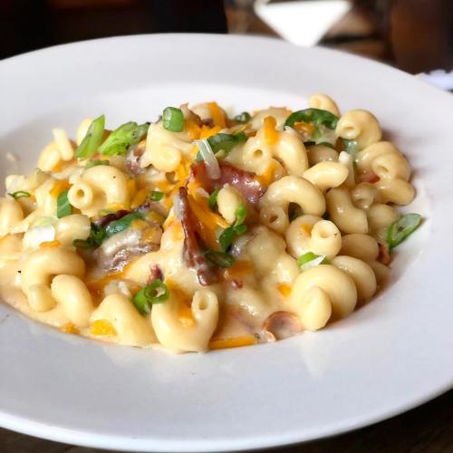 Creamy macaroni and cheese topped with bacon, cheddar, and green onions on a white plate.