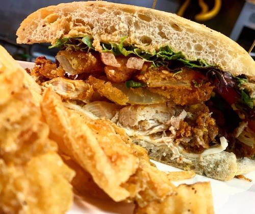 Close-up of a crispy chicken sandwich with lettuce, tomato, and fried onions, served with golden, crispy fries.