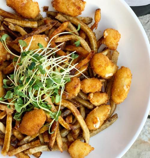 A plate of crispy fries topped with golden-brown bites and fresh microgreens.