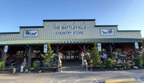 Exterior of The Battlefield Country Store, featuring a green roof, signage, and outdoor seating with decorative elements.