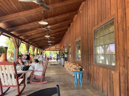 A rustic wooden patio with fans, tables, and people enjoying the outdoor space. Logs stacked against the wall.