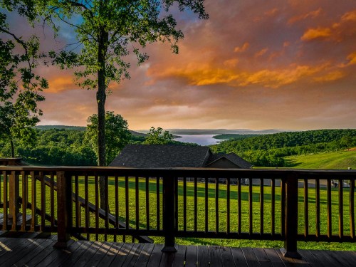Scenic view from a deck overlooking a lake, surrounded by lush greenery and a colorful sunset sky.